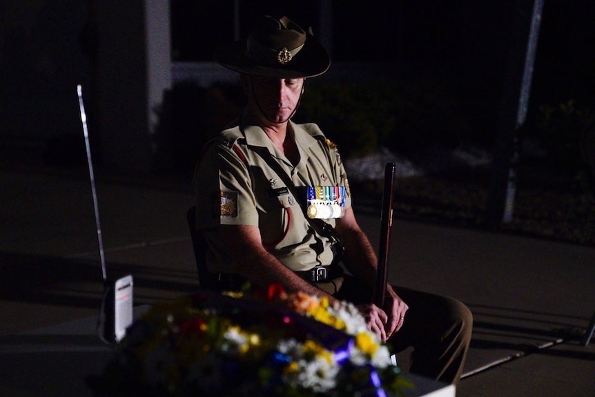 a man in army uniform sits on a chair next to a wireless radio with a wreath