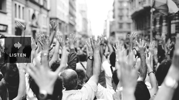 Black and white image shows a crowd standing with arms raised into the air and backs to the camera. . Has Audio.