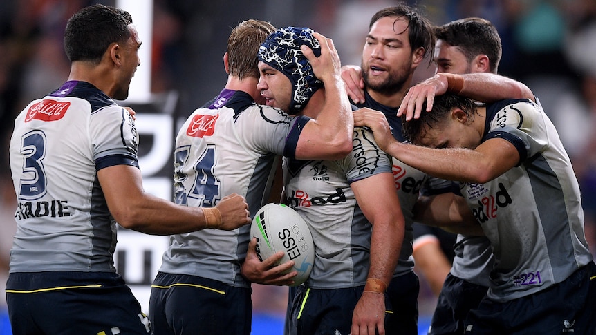 Six Melbourne Storm NRL players embrace as they celebrate a try against Wests Tigers.
