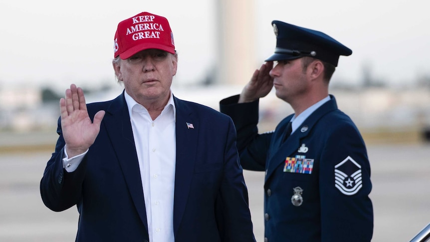 President Donald Trump waves as he steps off Air Force One wearing a hat that reads "Keep America great".