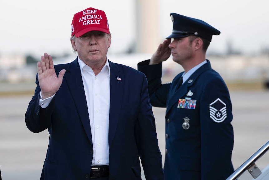 President Donald Trump waves as he steps off Air Force One wearing a hat that reads "Keep America great".