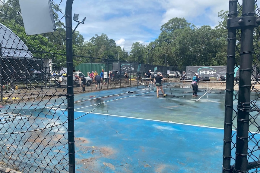 People cleaning tennis courts of flood debris.