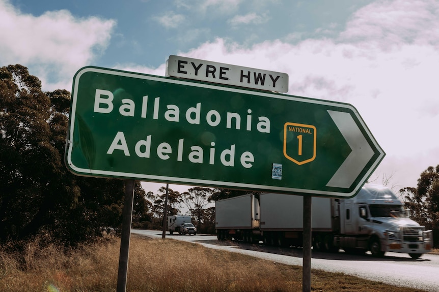 A road sign as a road train drives past.   