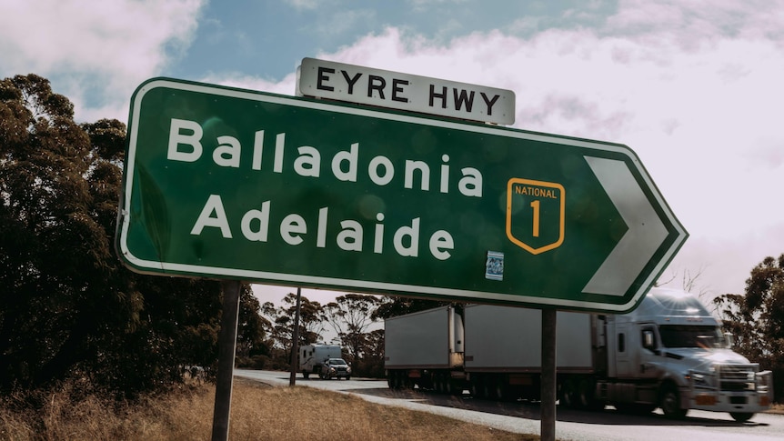 A road sign as a road train drives past.   