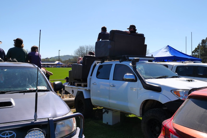 Fans sit in two couches stacked in the tray of a ute and on its roof