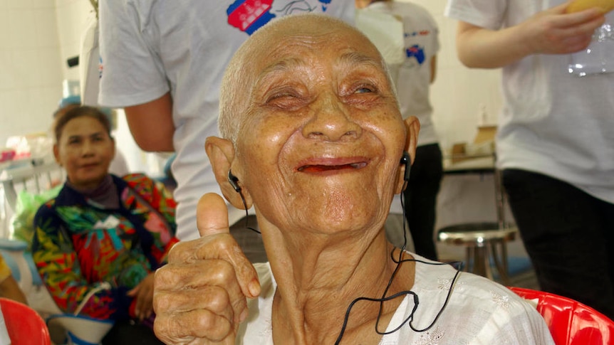An elderly Cambodian woman gives the thumbs up sign after receiving a hearing aid.