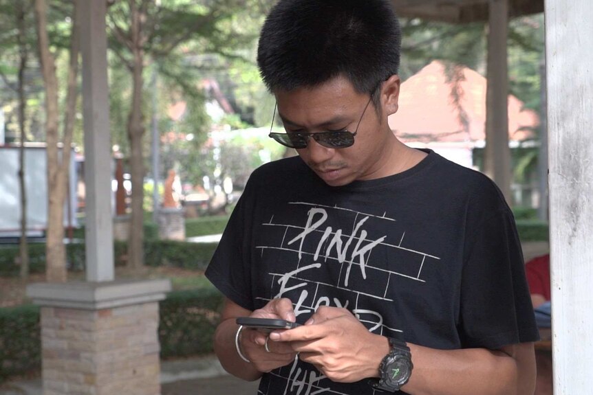 Law student Jatupat Boonpattararaksa wears a Pink Floyd shirt and looks down at his phone.