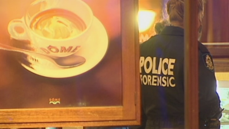 Image of a dome coffee cup in the foreground with a police officer in the background examining scene at cafe.