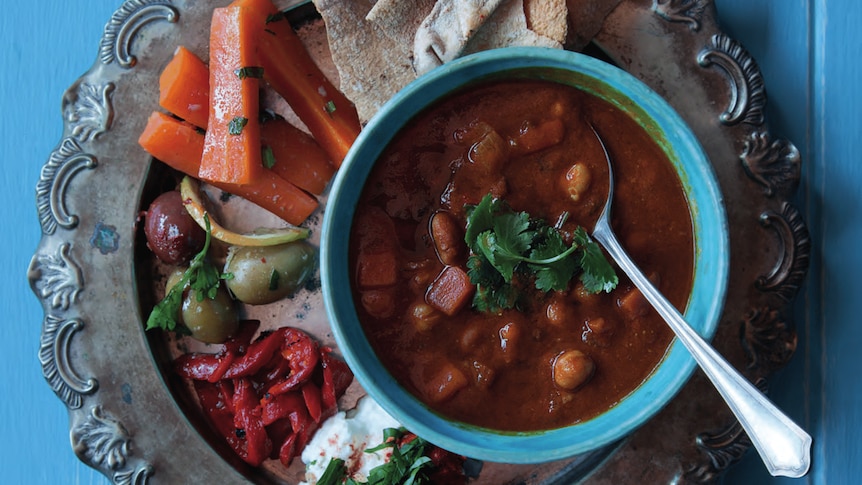 Harira soup in blue bowl with assorted pickled veg, feta and pita on blue table.