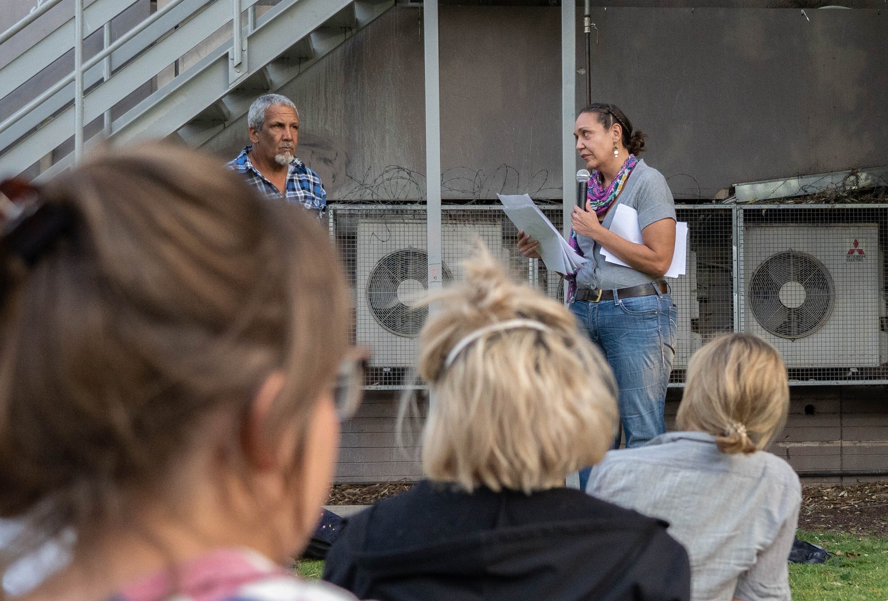A woman talks into a microphone in front of a crowd.