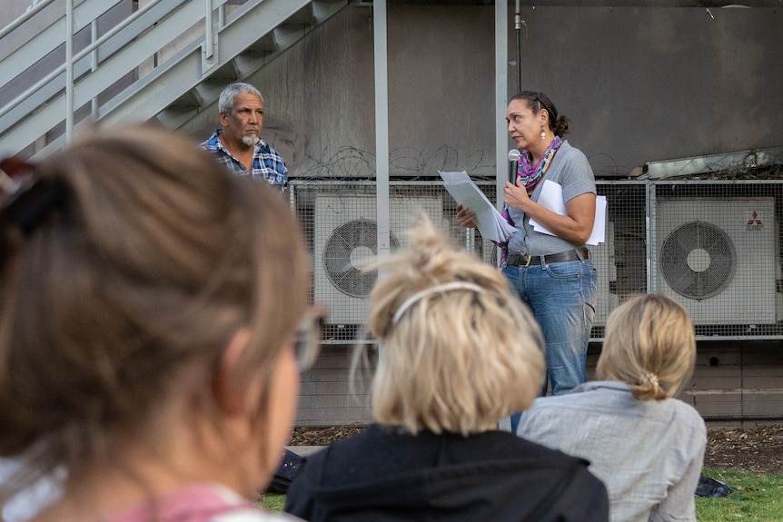 A woman talks into a microphone in front of a crowd.