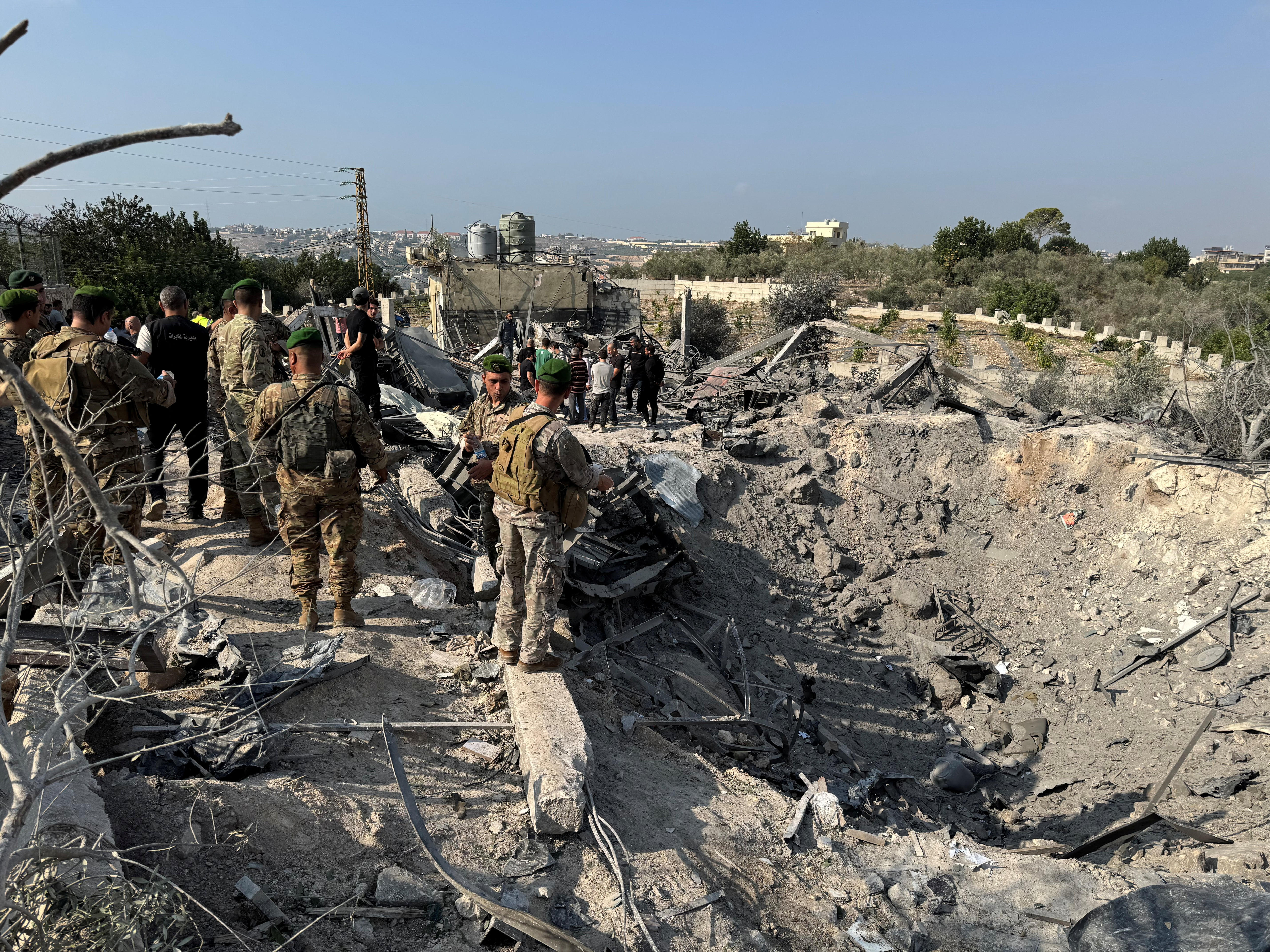 People, some in military uniform, gather on the side of a crater