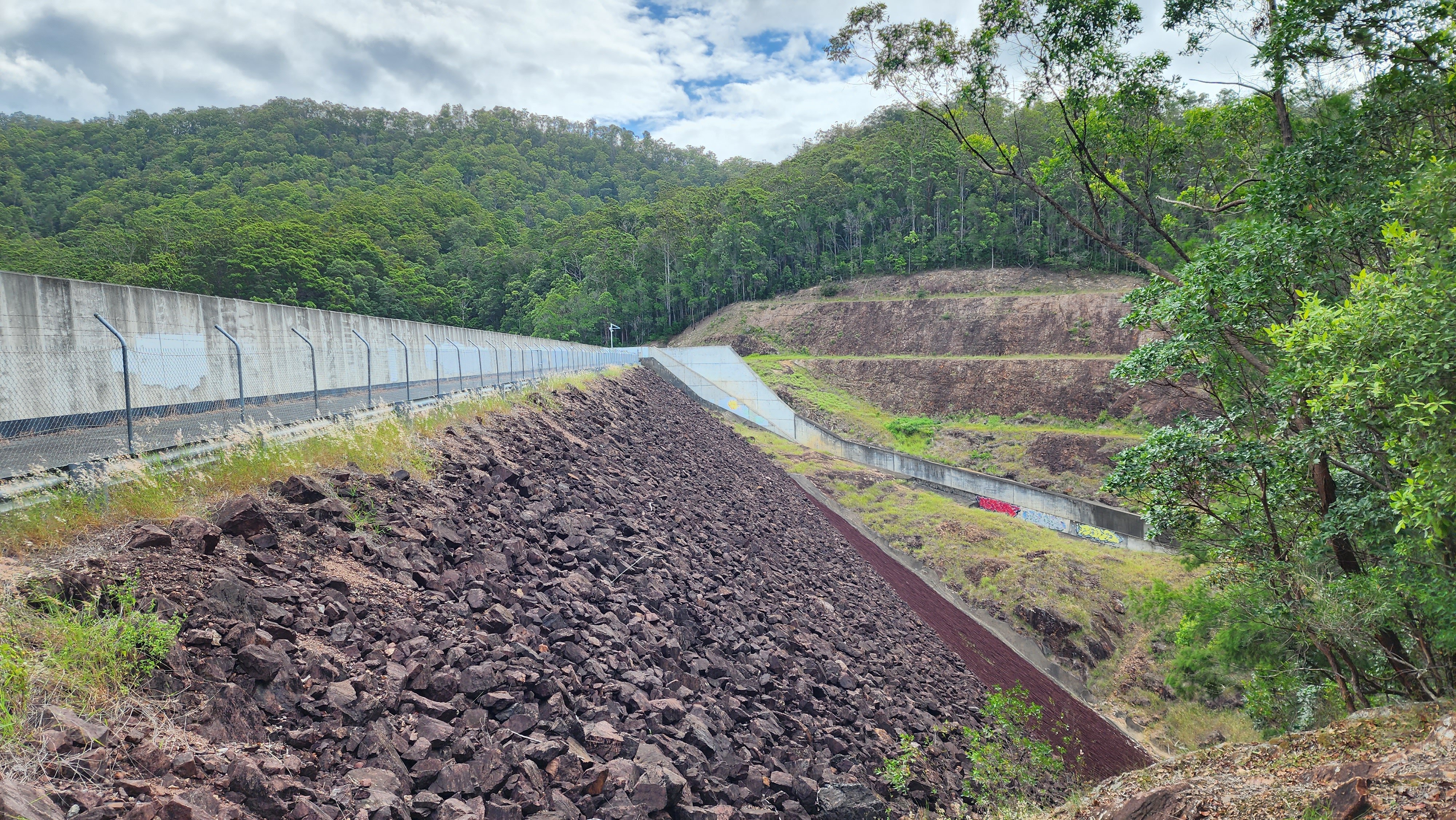 A concrete wall at the top of a slope covered in rocks which form the spillway.