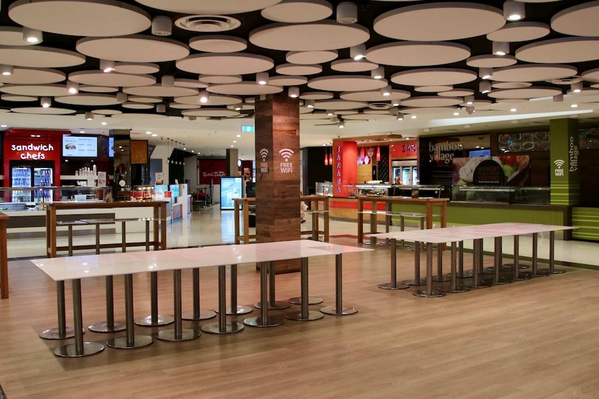 Tables are pushed side-by-side in an empty food court.