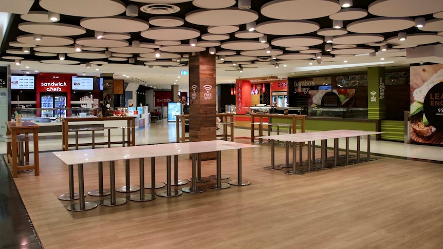 Tables are pushed side-by-side in an empty food court.