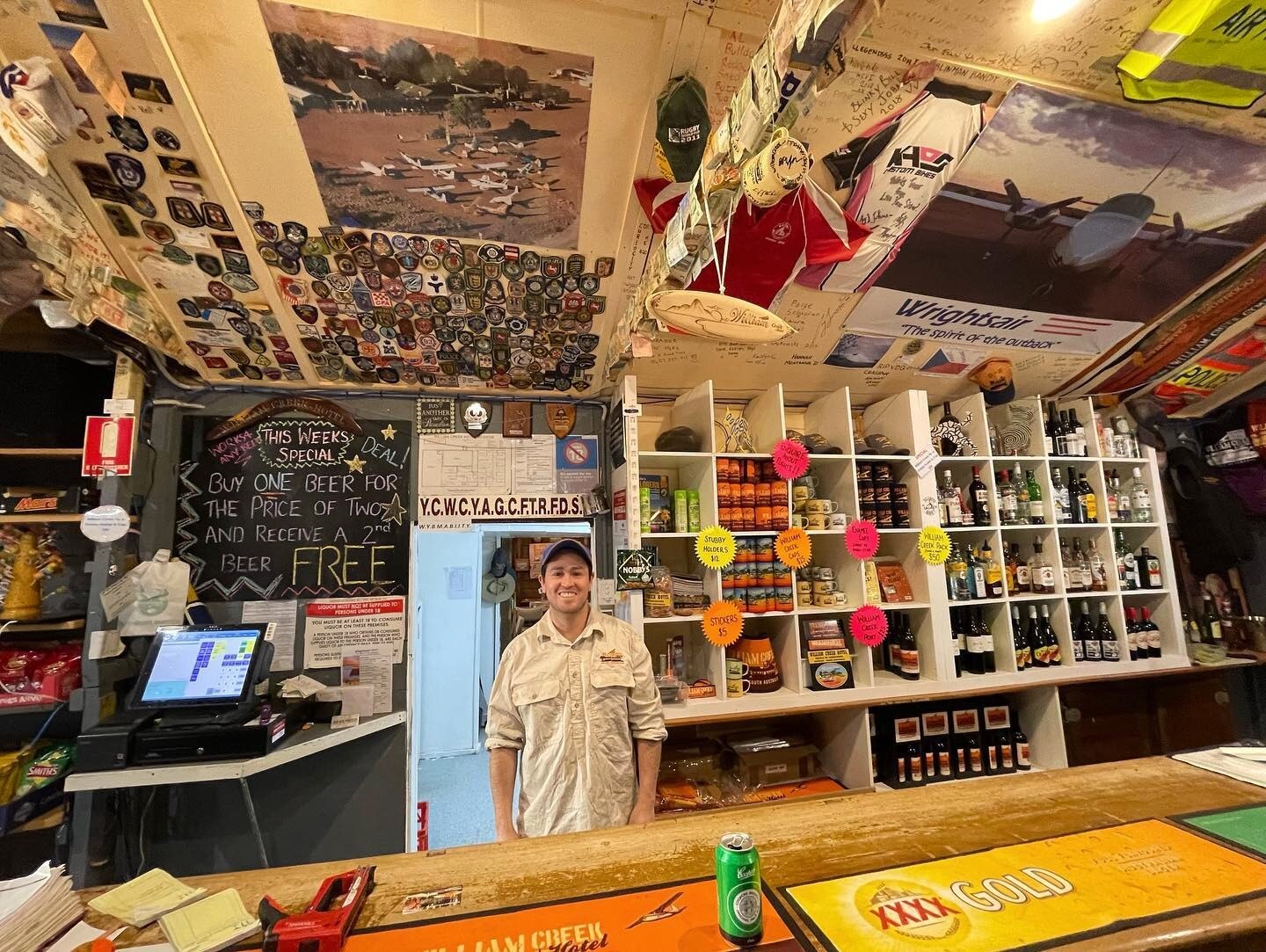 Man behind a bar filled with memorabilia on shelves and ceiling