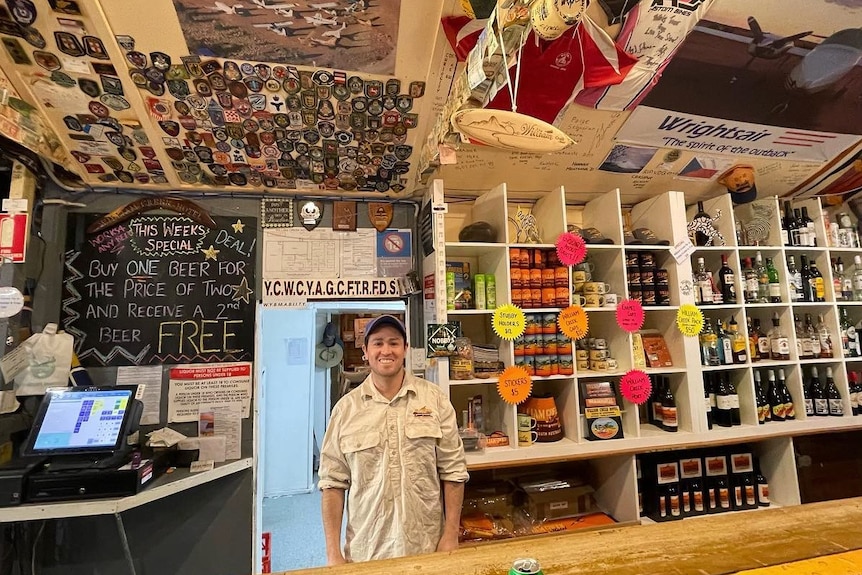 Man behind a bar filled with memorabilia on shelves and ceiling