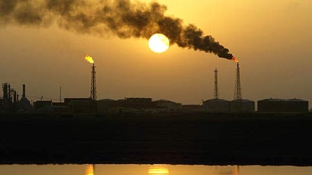 Smoke rises from Iraqi refinery al-Shouayba in Basra at sunset, reflected in an oil field.