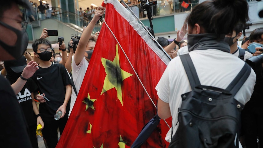 Protesters vandalise a Chinese national flag during a protest at a mall in Hong Kong. The flag is covered in black spray paint.