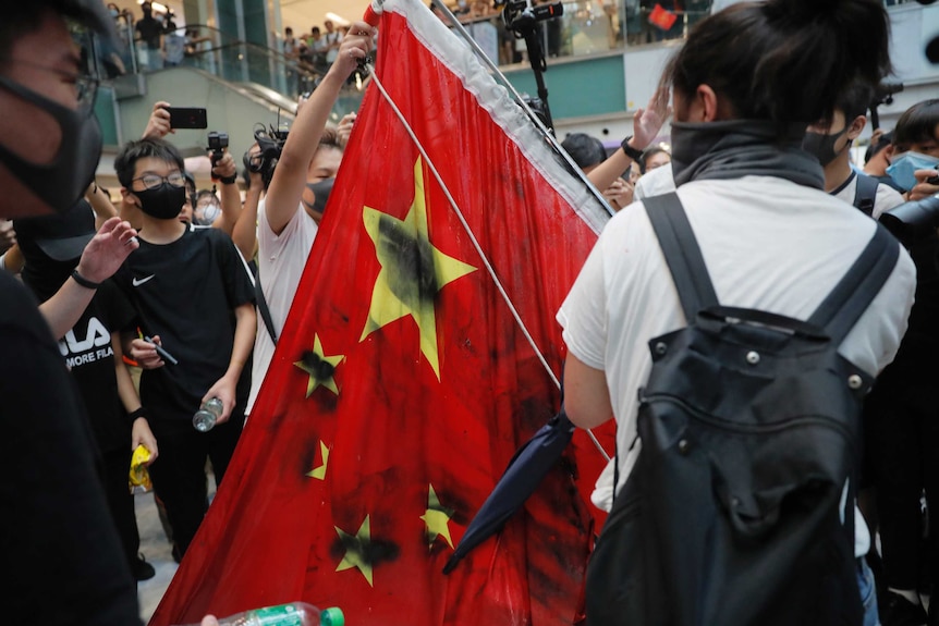 Protesters vandalise a Chinese national flag during a protest at a mall in Hong Kong. The flag is covered in black spray paint.