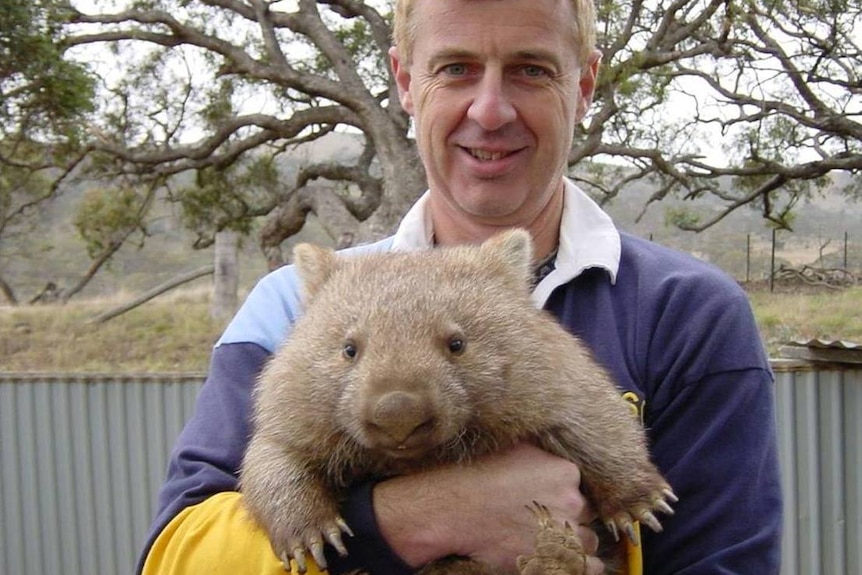 A man smiles at the camera and holds a fat wombat.