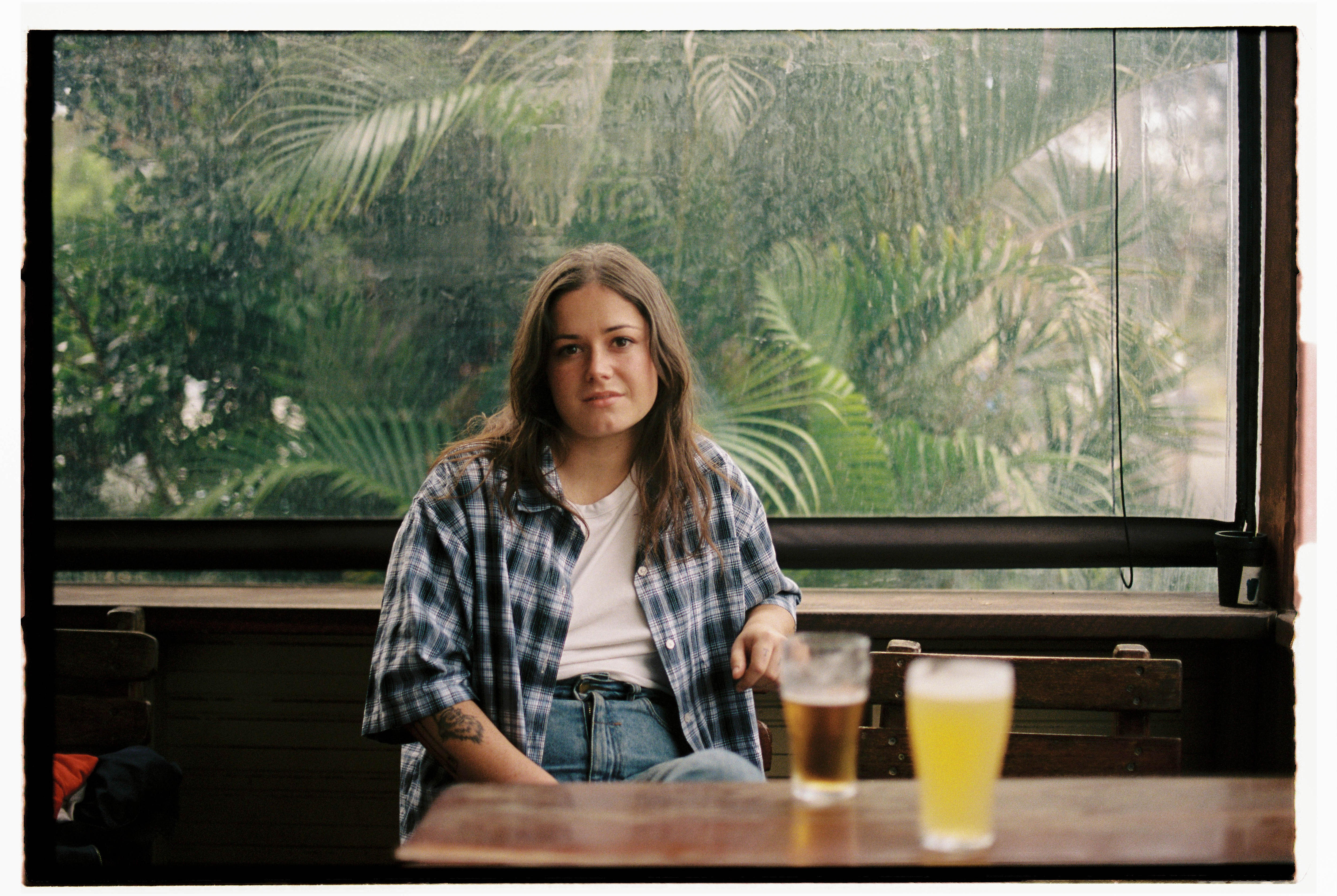 Ruby Fields sits at a pub table in a white shirt and blue plaid button up with two beers in front of her