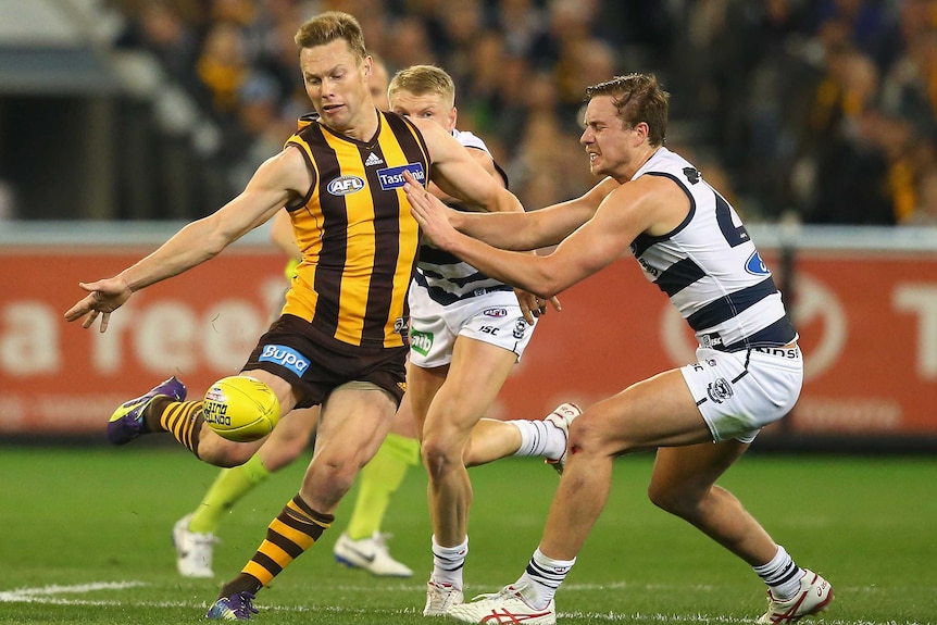 Hawthorn's Sam Mitchell kicks while Geelong's Mitch Duncan attempts to smother at the MCG.
