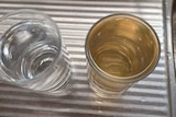 two glasses of water side by side one with brown water and the other with clear water