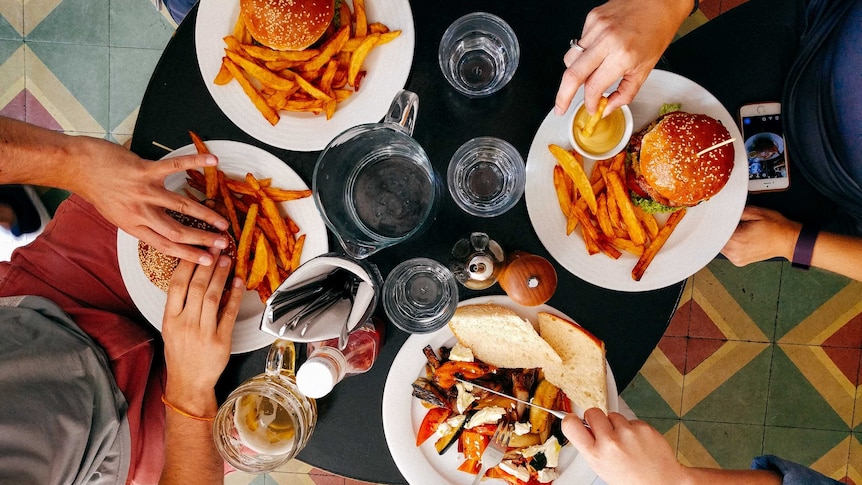 Four white plates with burgers, fries and salad on a black circular table from above