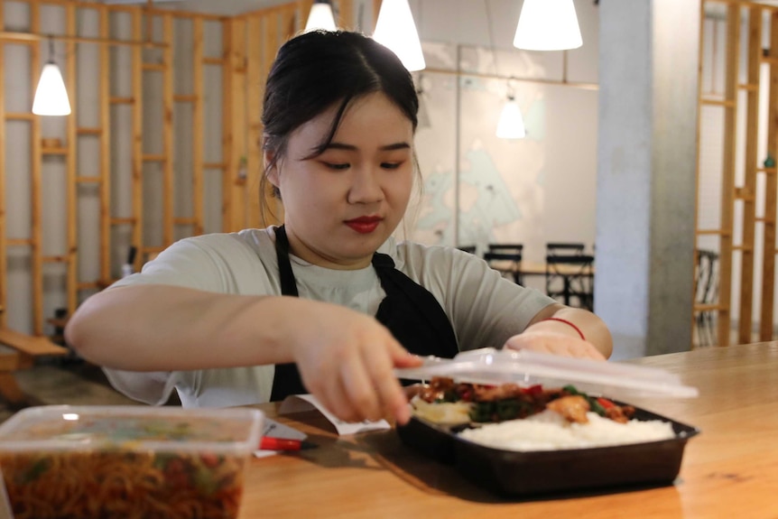 A waitress boxes up a Chinese meal in a plastic container in a restaurant.