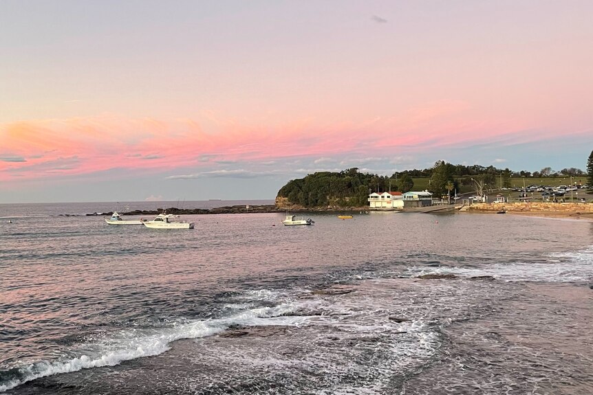 Pink skies over a beach with a house and boat in shot