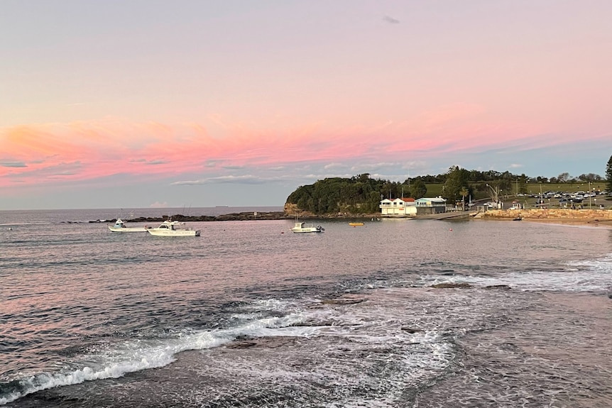 Pink skies over a beach with a house and boat in shot