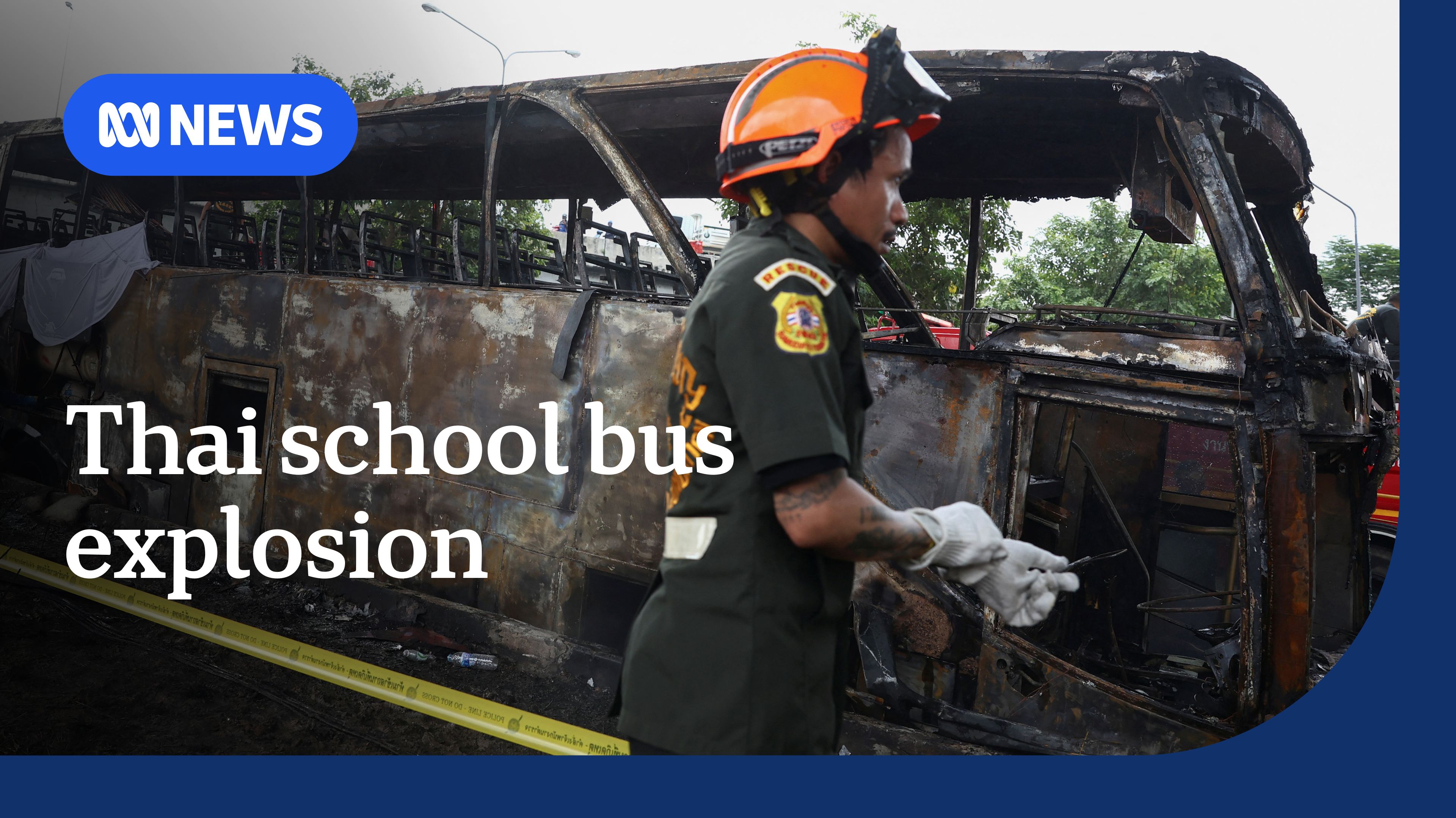 Thai School Bus Explosion: Charred and bare bus side on with an emergency worker walking past.