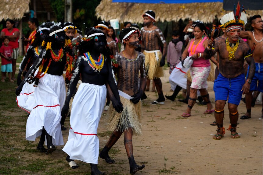 Boys and girls hold hands and walk in pairs while wearing traditional dress and body paint