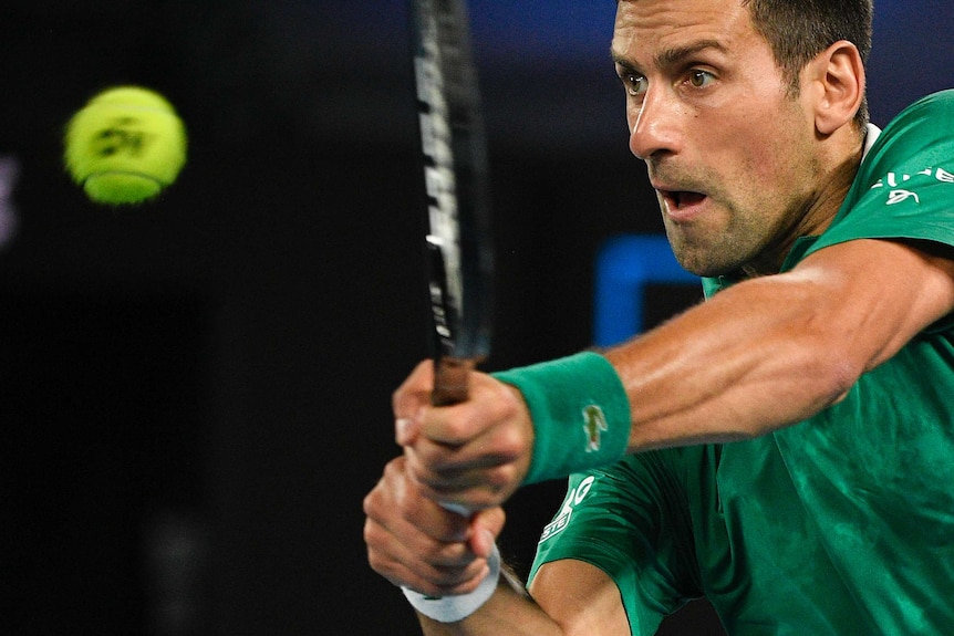 A tennis player brings his racquet forward to hit a backhand return.