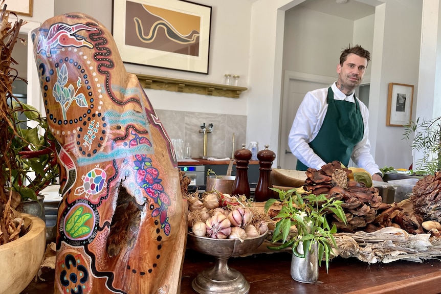 A man in a chef's apron looking at the camera with produce an Aboriginal art.