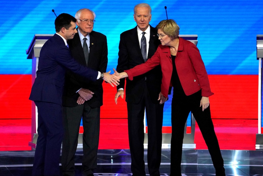 Pete Buttigieg and Elizabeth Warren shake hands in front of Bernie Sanders and Joe Biden