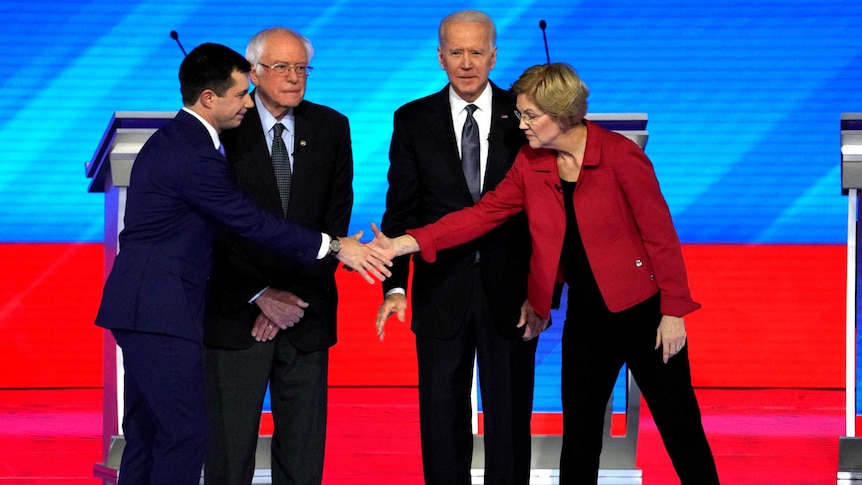 Pete Buttigieg and Elizabeth Warren shake hands in front of Bernie Sanders and Joe Biden