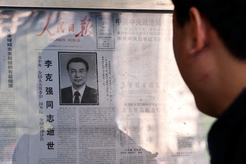 man reads newspaper showing obituary of li keqiang
