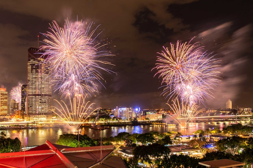 Fireworks explode over river, by a city