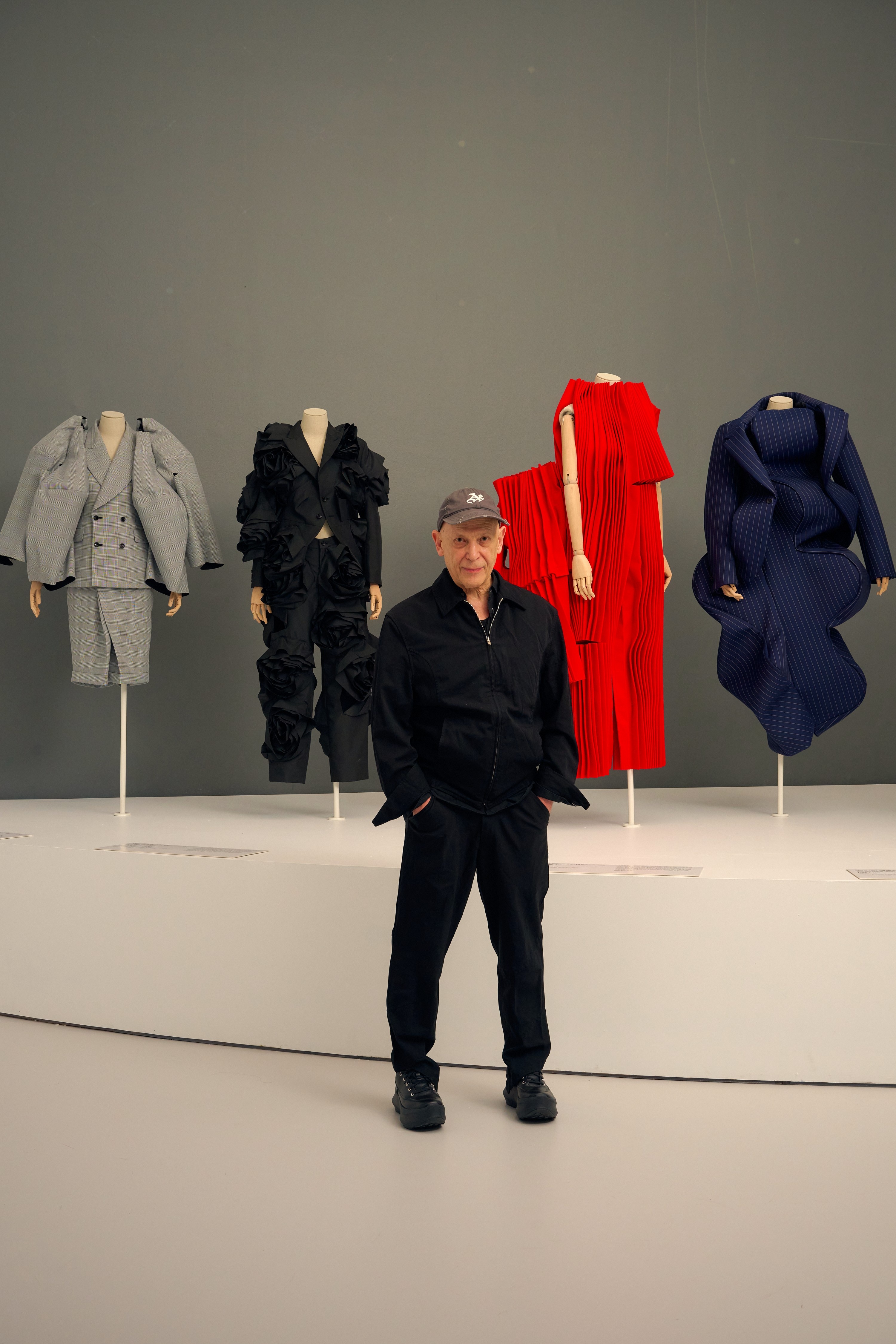 Adrian Joffe, con las manos en los bolsillos, en la exposición, delante de cuatro coloridos maniquíes con diseño Kawakubo