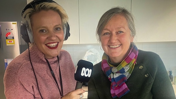 Jacinta in a pink jumper holds a mic to Caroline who is stirring porridge