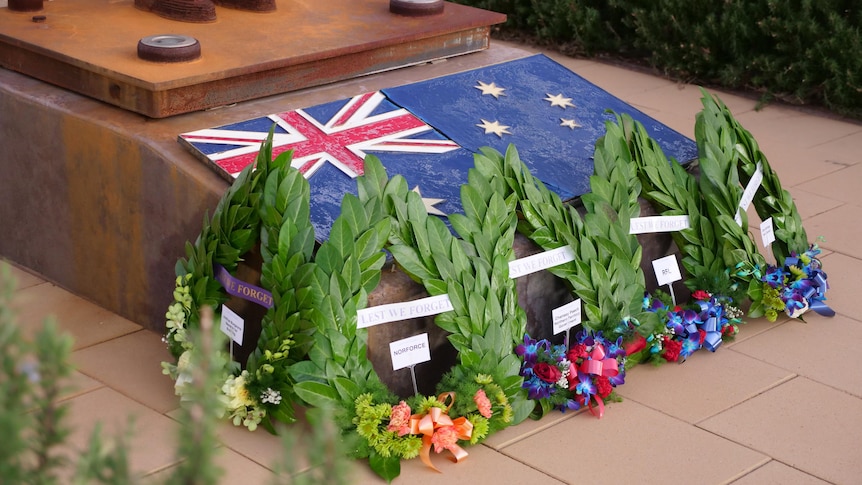 Several wreaths sit at the foot of a war memorial. 