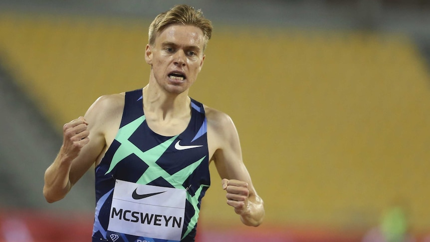 A runner clenches fists in celebration after winning a middle-distance event at an athletics meet.