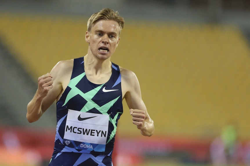 A runner clenches fists in celebration after winning a middle-distance event at an athletics meet.