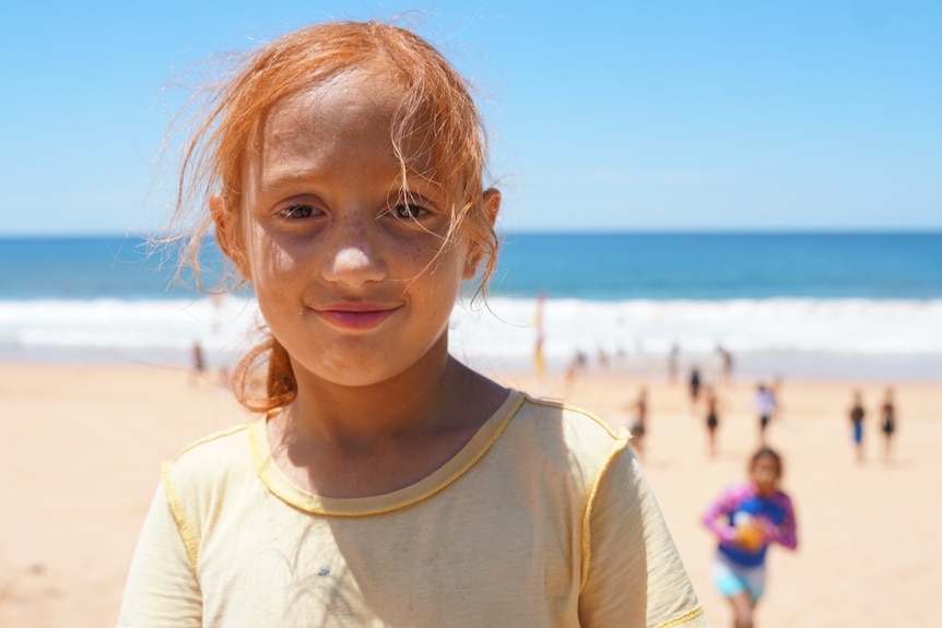 A young girl with red hair smiles on a beach