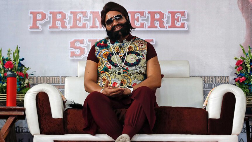 Rahim Singh sits on a couch. He is wearing sunglasses and a colourful vest. He is bearded and rotund.