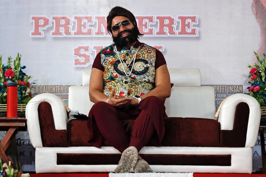 Rahim Singh sits on a couch. He is wearing sunglasses and a colourful vest. He is bearded and rotund.