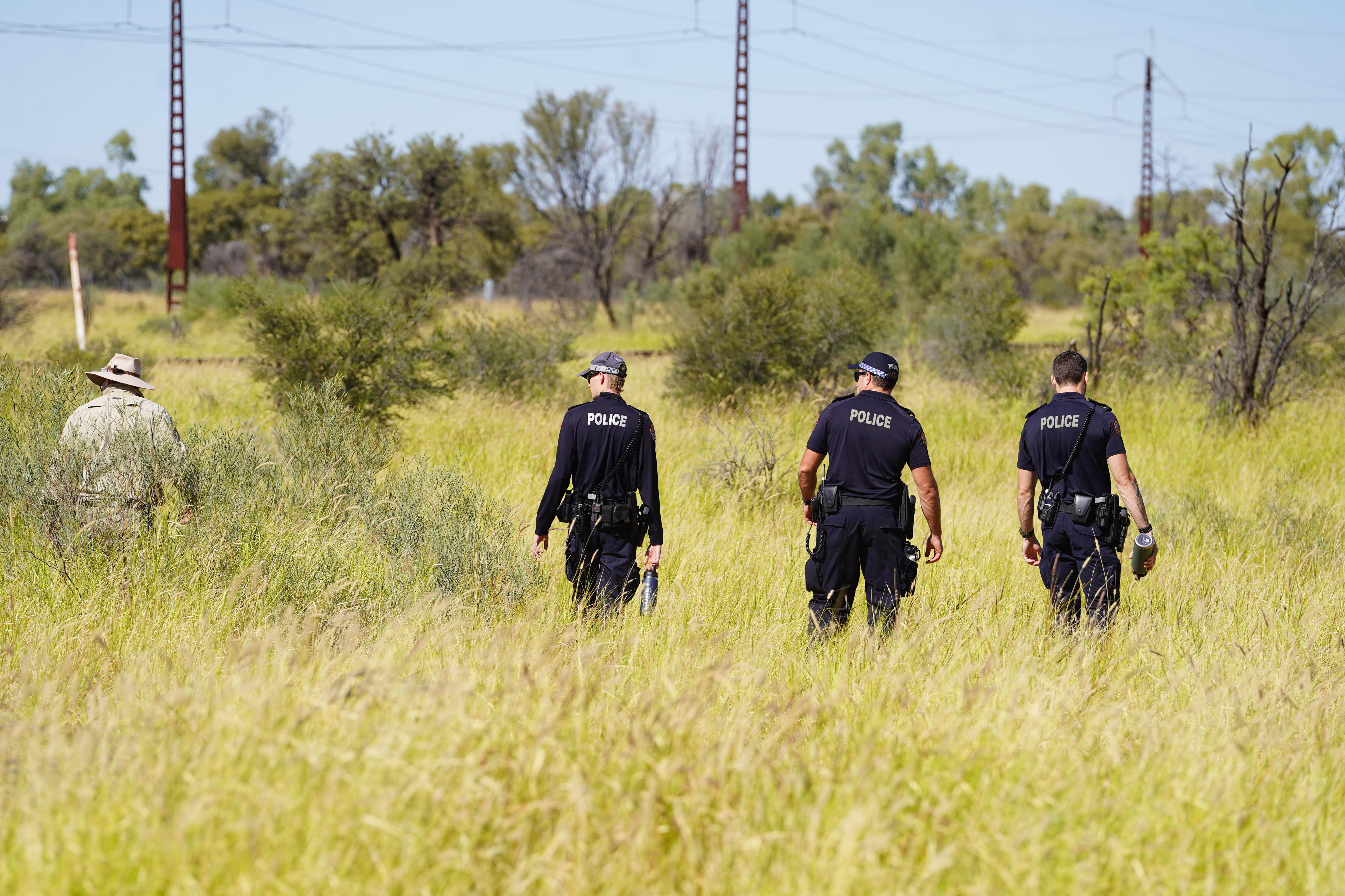 Police walk away from the camera as they search grassland