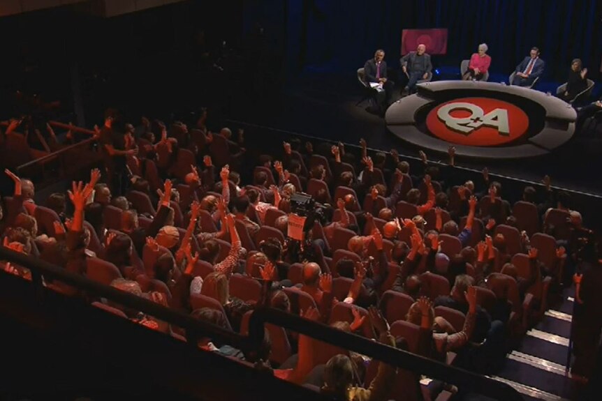 Audience members on the Q+A set raise their hands